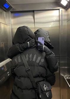 a person in a black jacket is looking at their cell phone while standing in an elevator