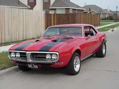 a red and black muscle car parked on the side of the road in front of a house