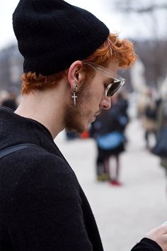 a man with red hair wearing sunglasses and a beanie looking at his cell phone