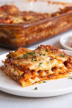 a white plate topped with lasagna next to a casserole dish