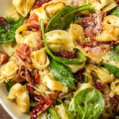 a white bowl filled with pasta, spinach and other toppings on top of a wooden table