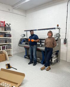 two people standing next to each other in a room filled with boxes and equipment, one holding an orange