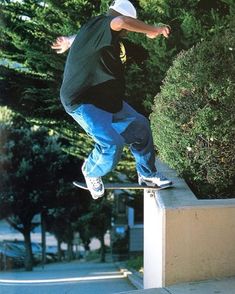 a man riding a skateboard down the side of a cement wall next to trees