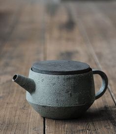 a gray teapot sitting on top of a wooden table next to a black cup