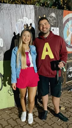 a man and woman standing next to each other in front of a wall with letters on it