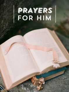 an open book sitting on top of a rock with a pink ribbon tied to it