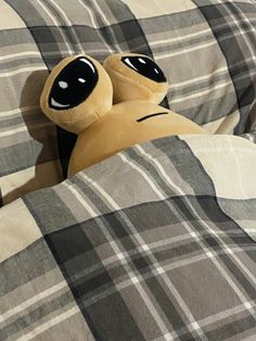 a stuffed animal laying on top of a bed covered in plaid sheets with eyes closed