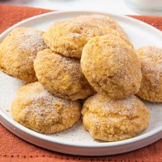 a white plate topped with sugar covered donuts on top of a red cloth next to a cup of coffee