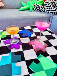 three glasses are sitting on a checkered tablecloth with colorful puzzle pieces in front of them