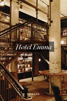 the inside of a hotel with stairs and tables in front of bookshelves filled with books