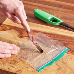 a person cutting paper with a knife on top of a wooden table next to scissors