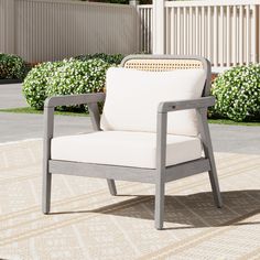 a white chair sitting on top of a rug in front of a fence and bushes