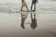 two people walking on the beach holding an umbrella