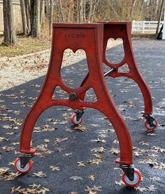 an old red metal chair sitting on top of a road next to leaves and trees