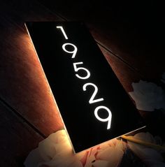 a lit up sign sitting on top of a wooden floor next to flowers and candles