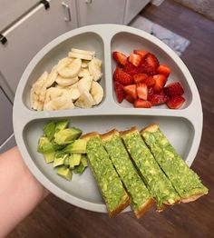 a person holding a plate with two sandwiches and fruit on it in front of them