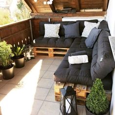 a couch sitting on top of a wooden pallet next to potted plants in front of a window