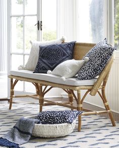 a wicker bench with several pillows on it in front of a large open window