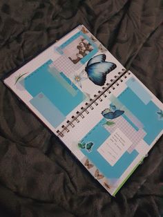 an open notebook with butterflies on it sitting on top of a black bed spreader