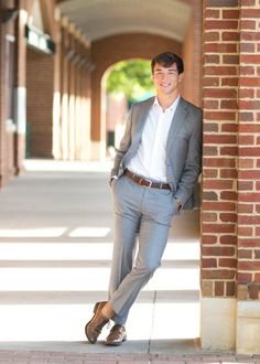 a man in a suit leaning against a brick wall with his hands in his pockets