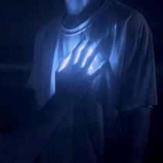 a man holding his hands up in the dark with glowing light on it's chest