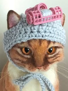 a cat wearing a crocheted hat with a pink hair comb on it's head