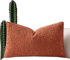 an orange and white pillow sitting next to a cactus