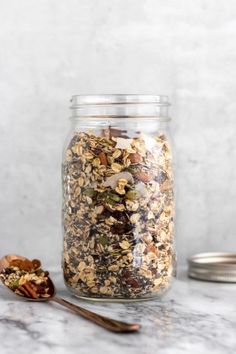 a glass jar filled with granola next to a spoon on top of a marble counter