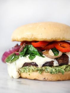 a sandwich with meat, cheese and vegetables on it sitting on a counter top in front of a white background