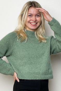 a woman in a green sweater is posing for the camera with her hands on her head