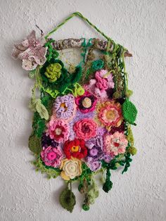 a crocheted bag with flowers hanging from it's side on a wall