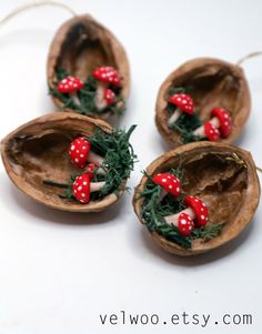 four small red mushrooms with green leaves in them on a white surface, set inside an egg shell