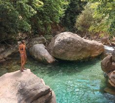 a woman standing on top of a large rock next to a river filled with water