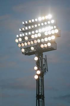 a tall light tower with lots of lights on it's sides and the sky in the background