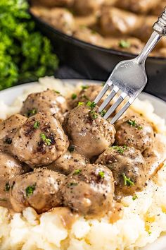 a plate with mashed potatoes, meatballs and gravy is being held by a fork