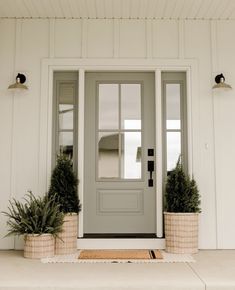 two potted plants sit on the front step of a white house with gray doors