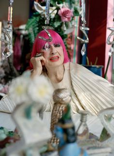 a woman with pink hair is sitting at a table and talking on her cell phone