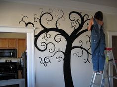 a woman painting a tree on the wall with black swirls and leaves in it