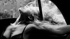 a black and white photo of a woman in a car looking out the side window