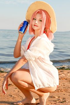 a woman with pink hair is sitting on the beach and holding a can in her hand