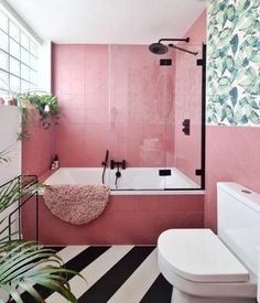 a bathroom with pink walls and black and white striped flooring, a bathtub, toilet and sink