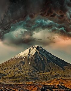 a large mountain covered in clouds under a sky filled with dark gray and white clouds