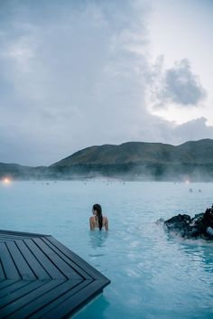 a woman sitting in the middle of a blue lagoon with steam rising from it's sides