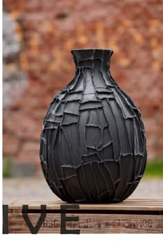 a black vase sitting on top of a wooden table in front of a brick wall