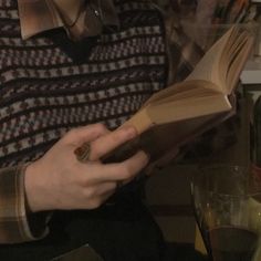 a person sitting at a table with an open book in their hands, reading it