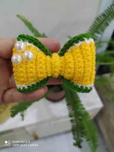 a hand holding a crocheted yellow bow tie with pearls on it's end