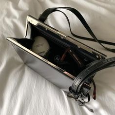 an open purse sitting on top of a white bed next to a black bag with two bottles in it