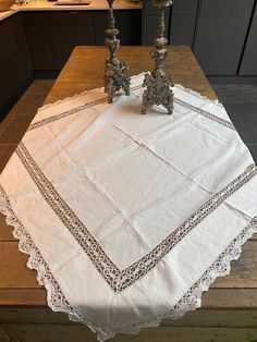 two candles are sitting on top of a white table cloth that has an intricate design