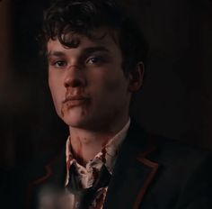 a young man with blood on his face and neck tie, looking at the camera