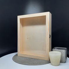 an empty wooden box sitting on top of a table next to a candle and container